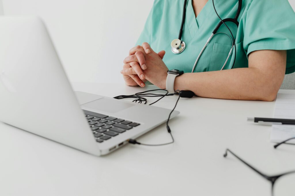 Medical professional in scrubs using a laptop for a remote telemedicine consultation, representing virtual healthcare support and hospital telemedicine services.