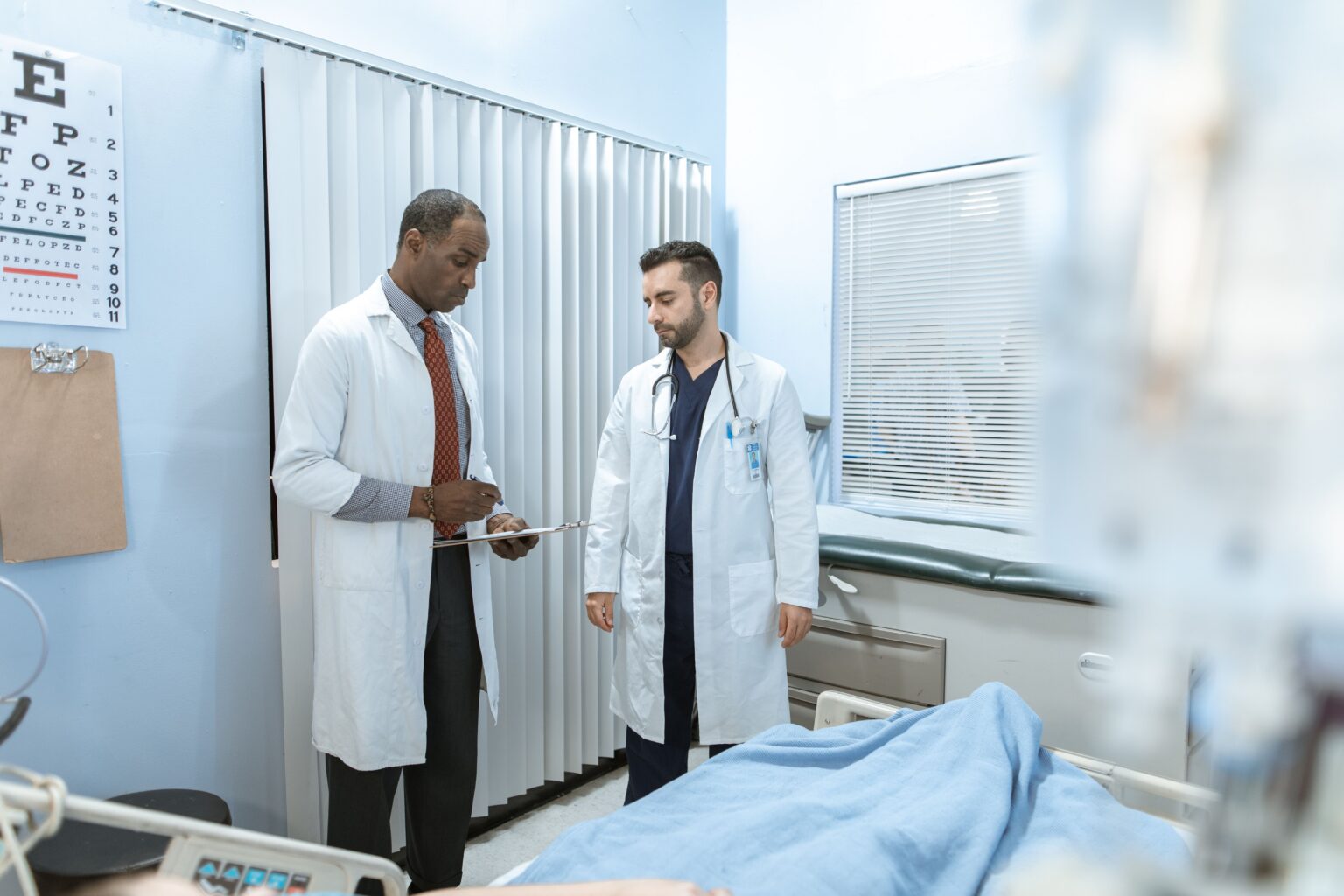 Doctors reviewing patient care in a hospital room, representing post-discharge follow-up, care coordination, and virtual specialty support.
